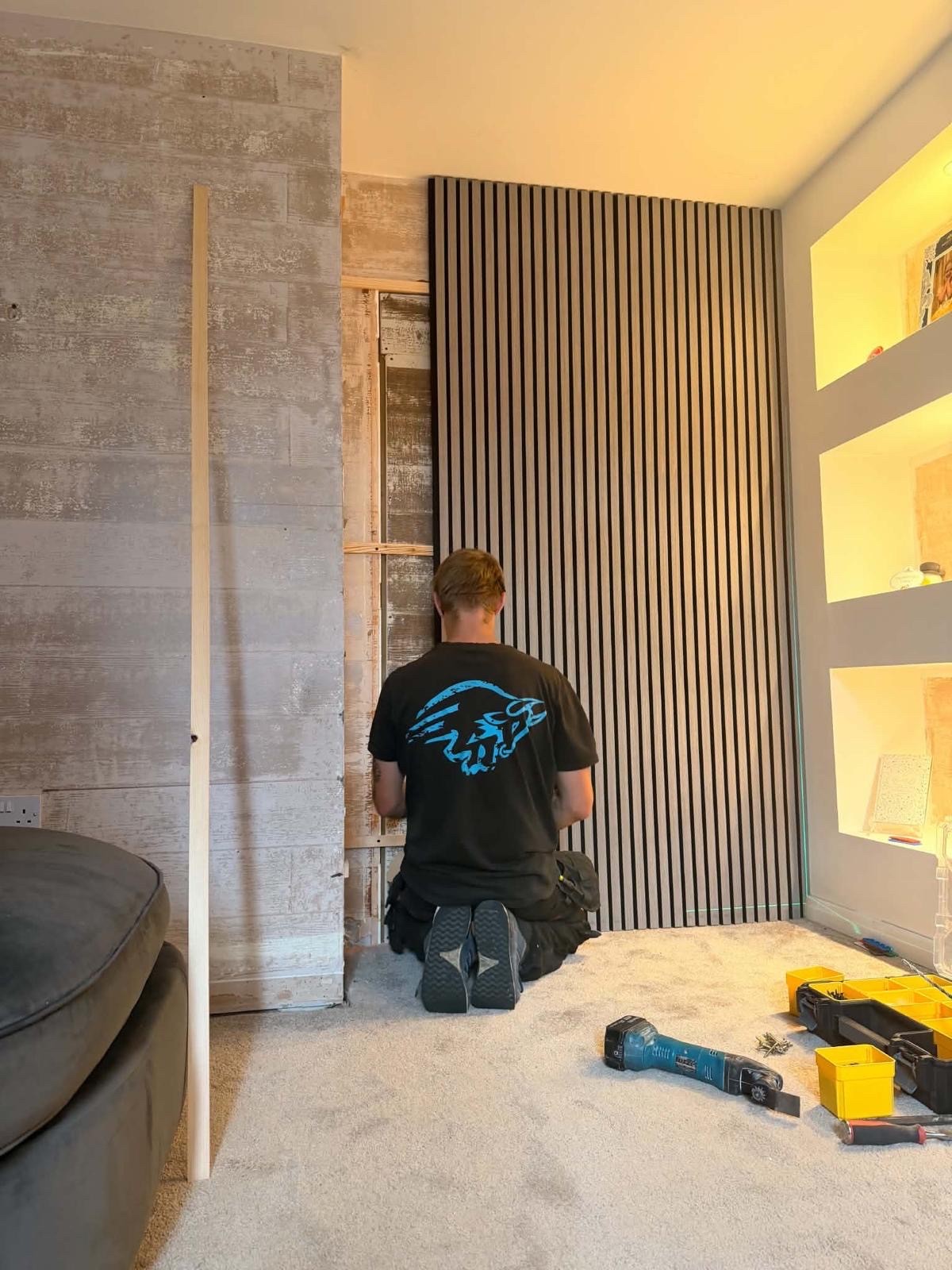 Ozz kneeling to fix the timber framework at the base of a newly installed slat panel wall