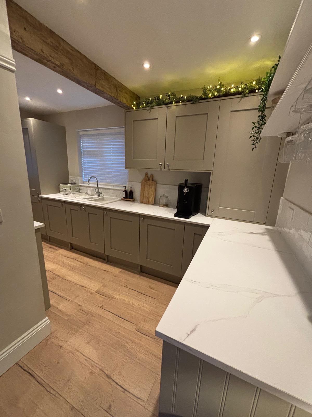 The same kitchen after the fit out: painted shaker cabinets, white quartz worktops, integrated appliances and oak-effect flooring